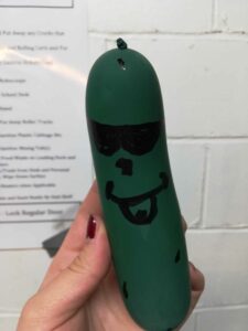 dark green balloon with sunglasses drawn on, held up in front of a white wall